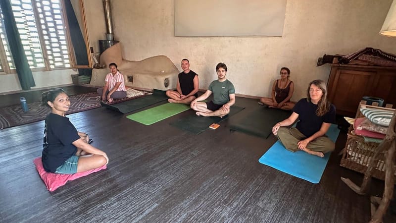 A small group sitting cross-legged on mats and cushions for a breathwork session in a farmhouse room