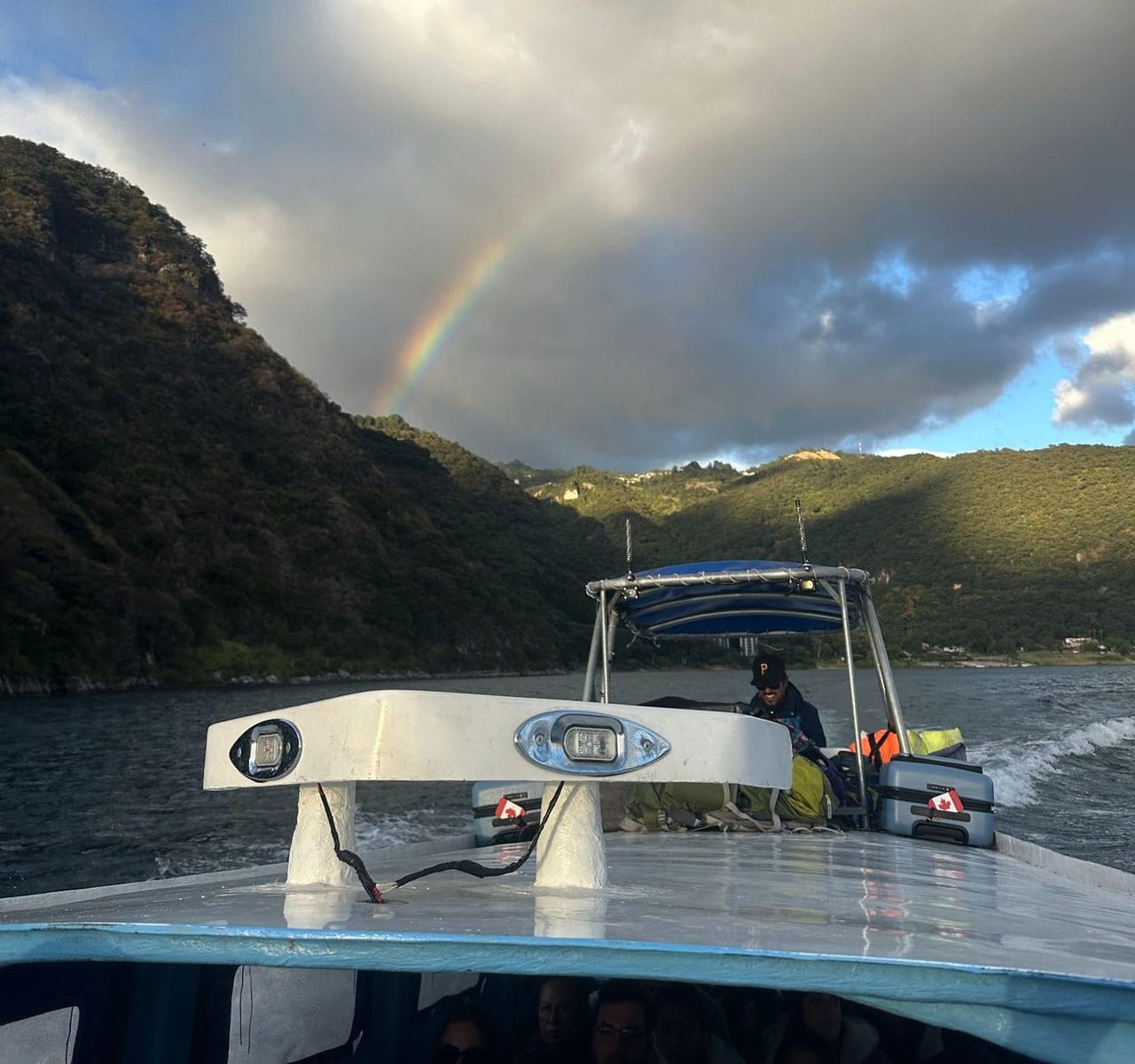 A rainbow arcing over Lake Atitlán's mountains, seen from the deck of a lancha crossing the water